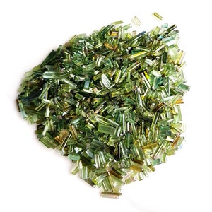 May include: A large pile of green and brown gemstone chips. The chips are long and thin, and they are scattered randomly on a white background.
