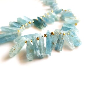 May include: A strand of light blue aquamarine crystal beads with gold accents. The beads are strung on a wire and are arranged in a cascading pattern.