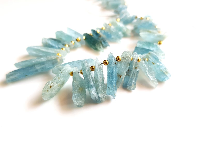 May include: A strand of light blue aquamarine crystal beads with gold accents. The beads are strung on a wire and are arranged in a cascading pattern.