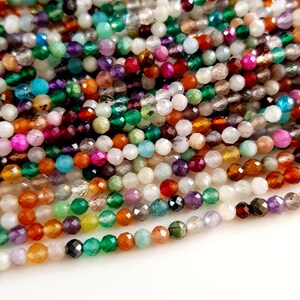 May include: A close-up shot of a collection of faceted gemstone beads in various colors. The beads are strung together, showcasing a diverse palette of hues including green, purple, orange, and white. These beads are suitable for jewelry making.