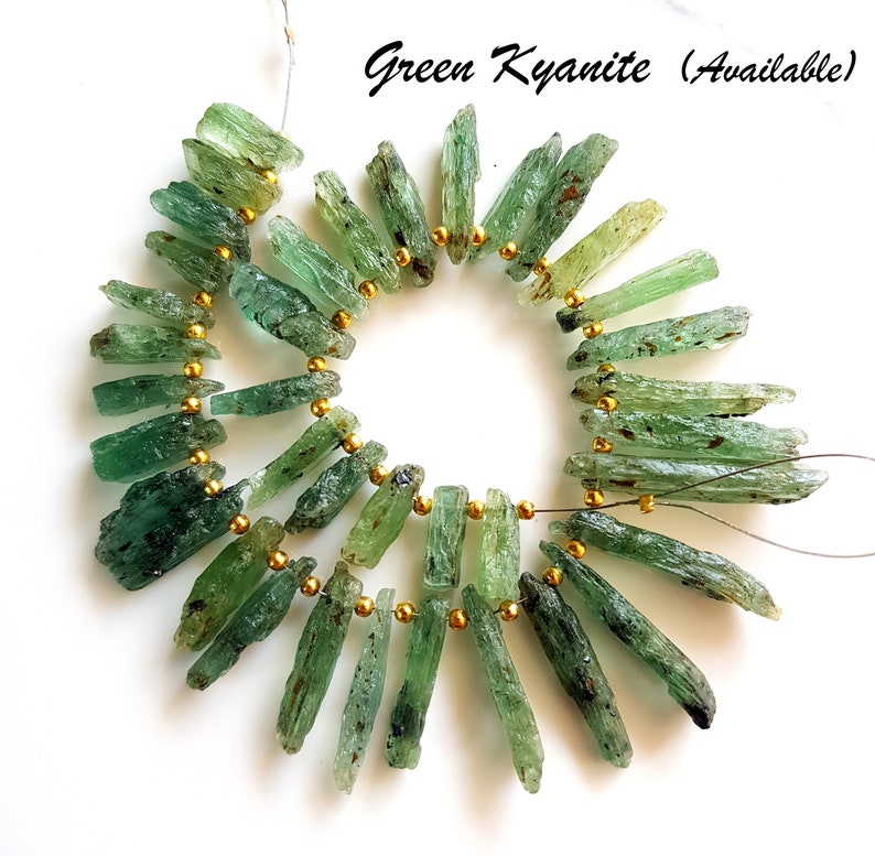 May include: A strand of green kyanite gemstone beads, strung on a wire with gold spacers. The beads are long and slender, with a natural, rough texture. Green Kyanite (Available)