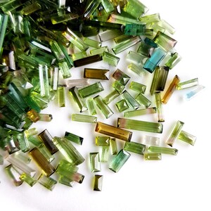 May include: A collection of green, blue, and brown gemstone chips in various sizes and shapes. The chips are scattered on a white surface.
