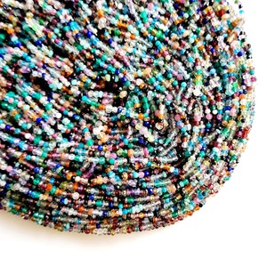 May include: A strand of colorful gemstone beads, including blue, green, purple, and brown, with a variety of shapes and sizes.
