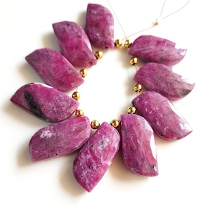 Puede incluir: Un collar de cuentas de piedras preciosas de rubí pulidas e irregulares. Las cuentas son de color rojo rosado intenso con algunas inclusiones más oscuras. Cada cuenta mide aproximadamente 2,5 cm de largo y está ensartada con cuentas espaciadoras doradas.