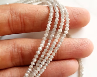 May include: A strand of white diamond beads, each bead is faceted and has a rough, irregular shape. The beads are strung on a clear thread and are arranged in a loose, flowing pattern.