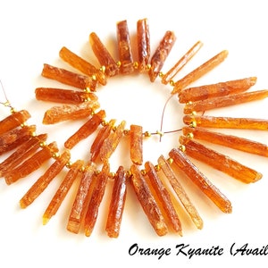 May include: A strand of orange kyanite gemstone beads, strung on gold wire. The beads are long and slender, with a natural, rough texture.  Orange Kyanite (Available)