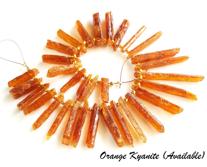 May include: A strand of orange kyanite gemstone beads, strung on gold wire. The beads are long and slender, with a natural, rough texture.  Orange Kyanite (Available)