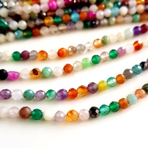 May include: Strands of faceted gemstone beads in a variety of colors, including green, orange, purple, and white. The beads are small and strung together, creating a colorful and textured appearance. Ideal for jewelry making.