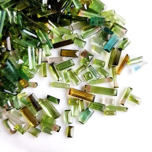 May include: A collection of green, blue, and brown gemstone chips in various sizes and shapes. The chips are scattered on a white surface.
