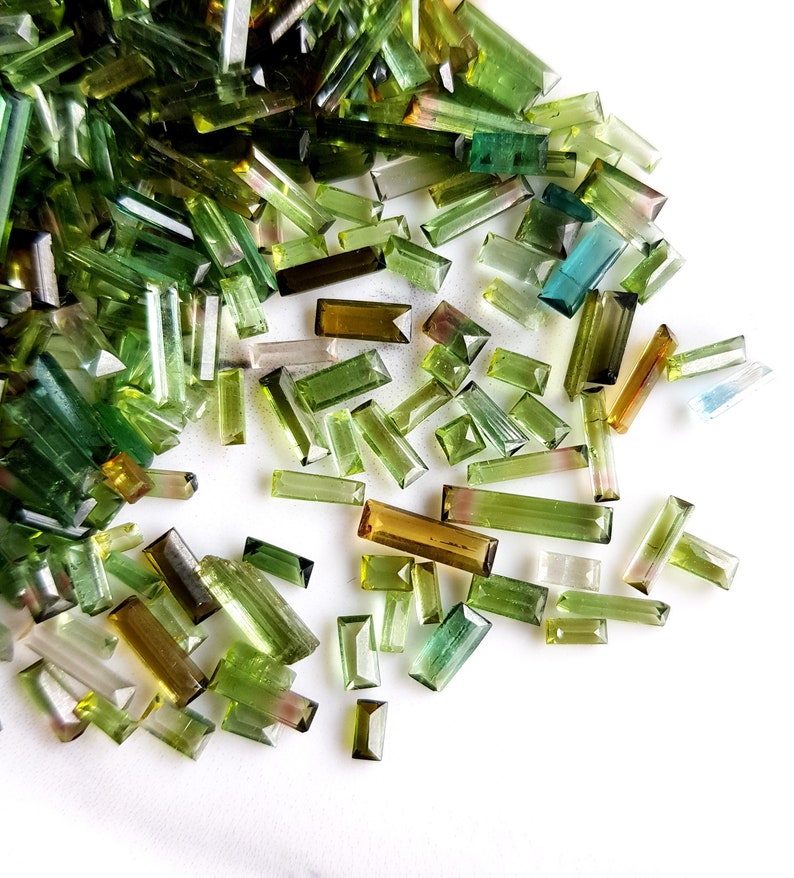 May include: A collection of green, blue, and brown gemstone chips in various sizes and shapes. The chips are scattered on a white surface.