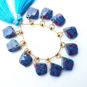 May include: A strand of blue and red gemstone beads with gold accents. The beads are faceted and have a unique, speckled appearance. The strand is strung on a gold chain with a blue tassel.