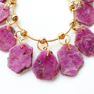 May include: A gold chain necklace with pink gemstone pendants. The gemstones are irregular in shape and have a rough, natural texture.