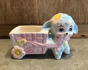 May include: A ceramic planter shaped like a lamb pulling a pink wagon with a yellow bird and flower accents.