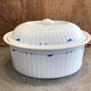 Puede incluir: Plato de cerámica blanco para hornear con un diseño floral azul y blanco. El plato tiene una tapa.