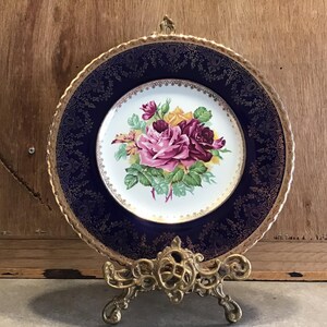 May include: A decorative plate with a gold rim and a blue background. The center of the plate features a floral design with pink, yellow, and red roses.