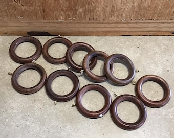 Könnte beinhalten: Zehn braune Holzvorhangringe mit goldenen Metallhaken. Die Ringe liegen verstreut auf einer grauen Oberfläche.