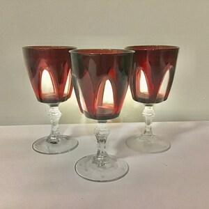 Può includere: Tre bicchieri da vino rosso con gambo e base in vetro trasparente. I bicchieri hanno un design unico con tagli nella coppa.