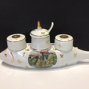 以下が含まれることがあります： 金色のアクセントが付いた白いセラミック製の魚型調味料セット。セットには、2つの塩入れ、蓋とスプーン付きの砂糖入れ、風景画が含まれています。金色の蝶が魚を飾っています。