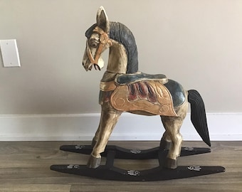 May include: A wooden rocking horse with a black mane and tail, painted in shades of brown, gold, and blue. The horse has a saddle with a red, gold, and blue design. The rocking base is black with white handprints.