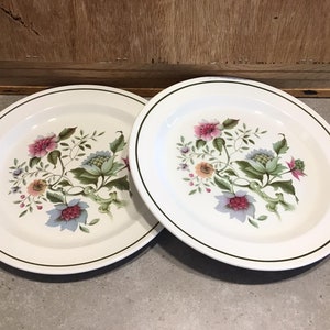 May include: Two white ceramic dinner plates with a green and floral design. The plates have a thin green rim.