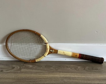 May include: A vintage wooden tennis racket with a white and yellow grip and a red and white Dunlop logo. The racket has a metal stringed frame.