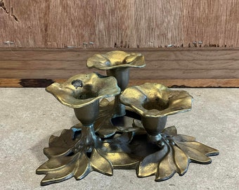 Könnte beinhalten: Ein goldfarbener Kerzenhalter aus Metall mit drei Kerzenbechern in Form von Blumen. Der Kerzenhalter ist mit Blättern verziert und hat ein florales Design.