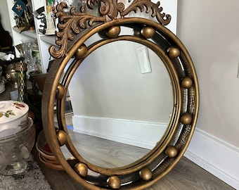 Könnte beinhalten: Runder, goldfarbener Spiegel mit dekorativem Rahmen. Der Rahmen weist goldene Kugeln und ein verziertes, floral inspiriertes Oberteil auf. Der Wandspiegel verleiht einen Hauch von Vintage-Eleganz. Der Durchmesser des Spiegels beträgt ca. 60 cm.