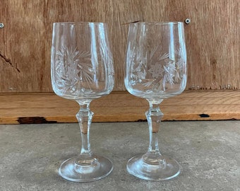 May include: Two clear glass wine glasses with a cut crystal design. The glasses have a tall stem and a round bowl.