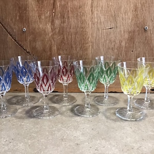 Puede incluir: Juego de ocho vasos de cristal transparente con tallo y diseños geométricos de colores. Los vasos tienen un diseño azul, rojo, verde y amarillo.