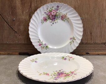 May include: Two white ceramic plates with a floral design. The plates have a scalloped edge and a gold trim. The flowers are pink, purple, and green.