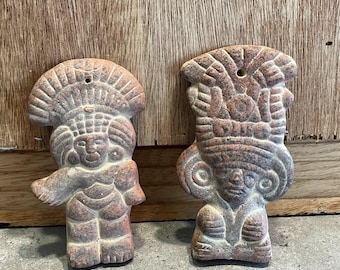 May include: Two terracotta figurines of people wearing headdresses. The figurines are carved with intricate details and have a reddish-brown color.