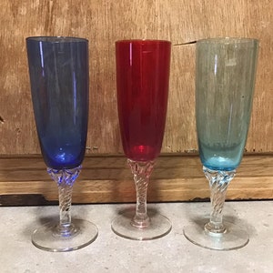 Könnte beinhalten: Drei Champagnergläser mit Stiel und gedrehten Stielen. Die Gläser sind blau, rot und grün.
