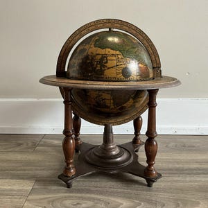 May include: An antique globe with a wooden stand. The globe features detailed cartography with various continents and oceans. The stand has four legs and a circular base. The globe is supported by a wooden frame with a curved meridian ring.