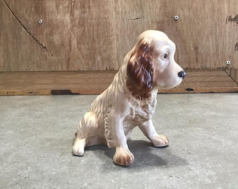 Peut inclure: Une figurine en céramique d'un chien brun et blanc assis, la tête tournée sur le côté. Le chien a des oreilles brunes et un nez noir.