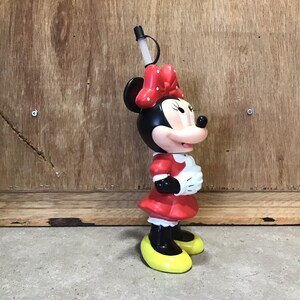May include: A Minnie Mouse-shaped tumbler with a black head, red bow, and red dress. The tumbler has a black straw and yellow shoes. The design is a classic Disney character.