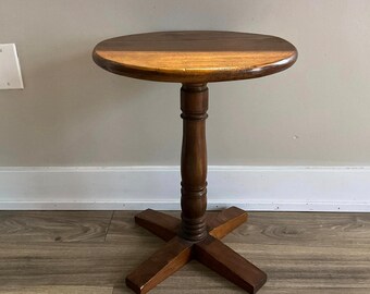 May include: A round wooden side table with a brown finish. The table has a single pedestal base with a cross-shaped foot.