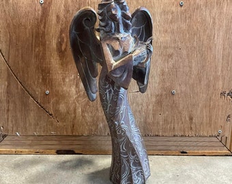 May include: A wooden angel figurine with wings, holding a musical instrument. The angel is painted in shades of brown and white with intricate details.