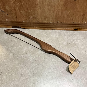 May include: A wooden bread knife with a stainless steel blade. The knife has a curved handle and a tag that reads "Appalachian Bread Slicer Handmade in the USA".