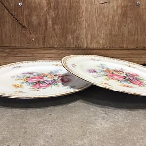 May include: Two white oval plates with a gold rim and a floral design in shades of pink, yellow, and purple.