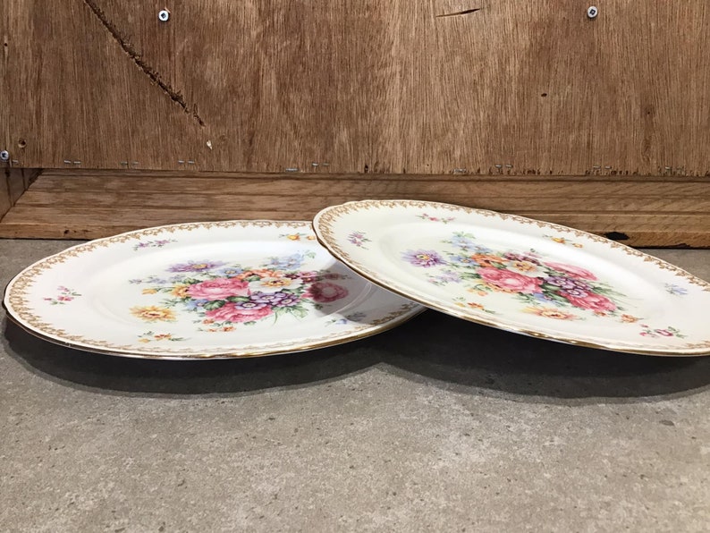 May include: Two white oval plates with a gold rim and a floral design in shades of pink, yellow, and purple.