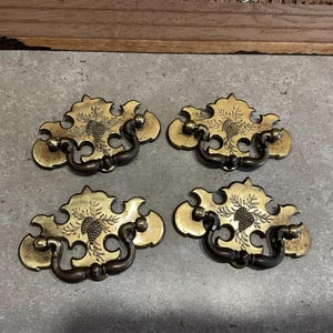 May include: Four antique brass cabinet pulls with a pine cone design. Each pull has a decorative, ornate shape and a simple, functional loop handle.