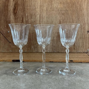 May include: Three clear glass wine glasses with a diamond pattern on the bowl and stem. The glasses are on a grey surface.
