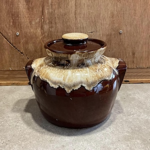 Könnte beinhalten: Ein brauner und weißer glasierter Keramik-Schmortopf mit zwei Griffen und einem Deckel. Der Schmortopf hat ein Tropf-Glazurmuster.