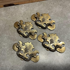 May include: Four antique brass cabinet pulls with a pine cone design. Each pull has a decorative, ornate shape and a simple, functional handle.