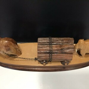May include: A wooden sculpture of two elephants pulling a log on a wooden base. The elephants are carved in a realistic style and the log is tied with a chain.
