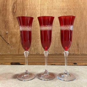 Könnte beinhalten: Drei rote Champagnergläser aus Glas mit einem klaren Kristallmuster um den Kelch. Die Gläser stehen auf einer hellbraunen Holzoberfläche.