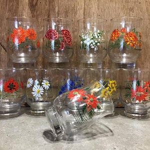 May include: Set of ten clear glass tumblers with floral designs. Each glass features a different flower with its name printed on the bottom. The flowers include a poppy, daisy, forget-me-not, daffodil, and poinsettia.