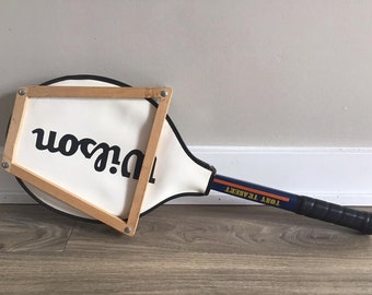 Könnte beinhalten: Ein Vintage-Wilson-Tennisschläger mit einem Holzrahmen und einem blau-orangenen Griff. Der Griff trägt den Schriftzug "Tony Trabert".