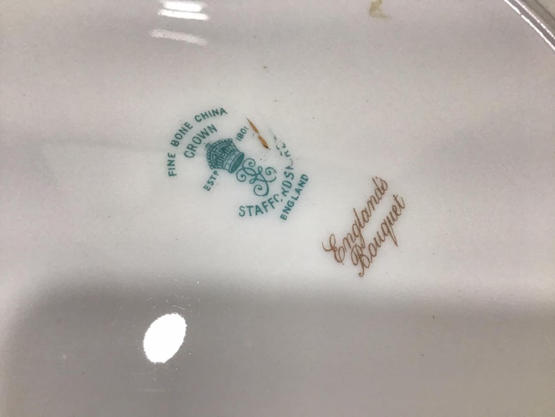 May include: Close-up of a white ceramic plate with a green and gold logo that reads "Fine Bone China Crown Est. 1801 Staffs.  Eng.  England's Bouquet".