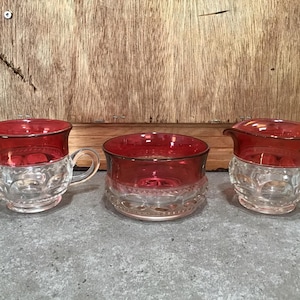 Puede incluir: Un juego de tres boles de azúcar y crema vintage de vidrio con un borde rojo rubí y una base de vidrio transparente. Los boles tienen un patrón decorativo.